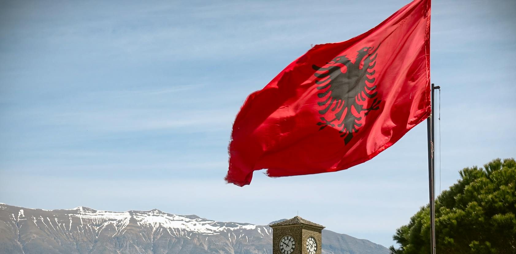 view of the albanian flag and the gjirokaster fortress with mountains in the background