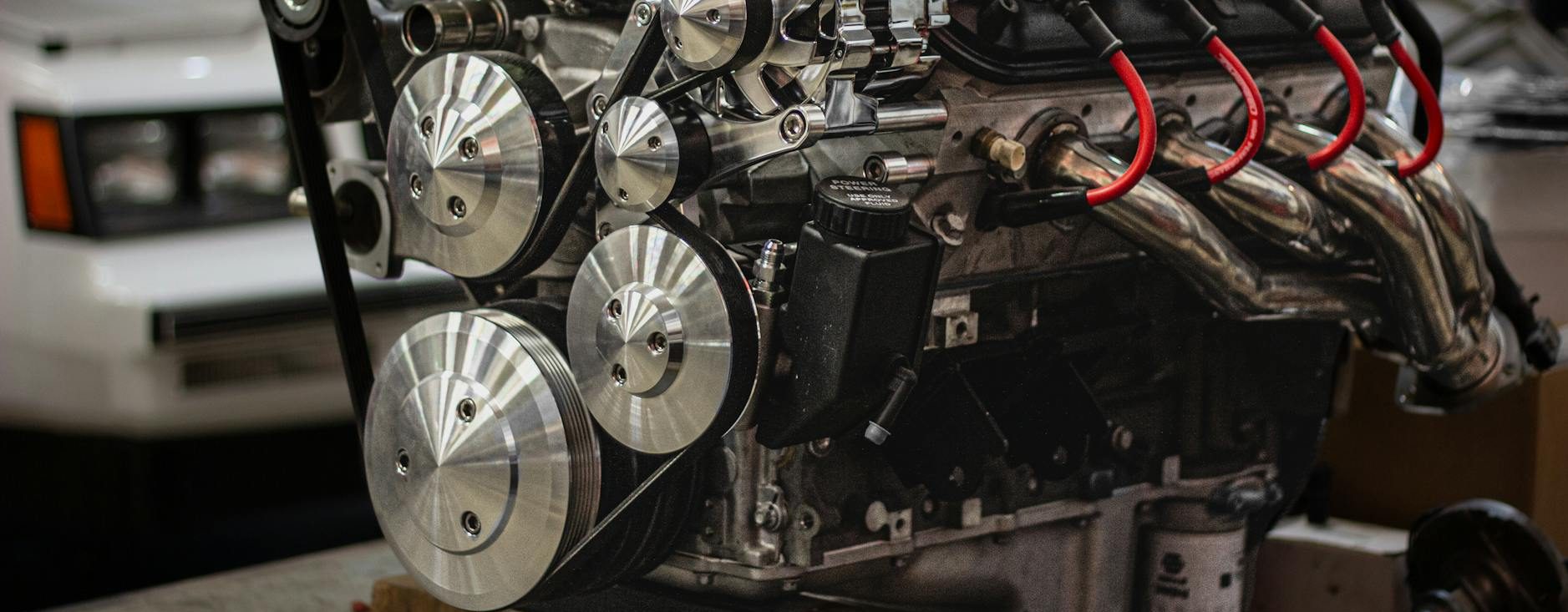 close up of an engine and a car in the background in a garage
