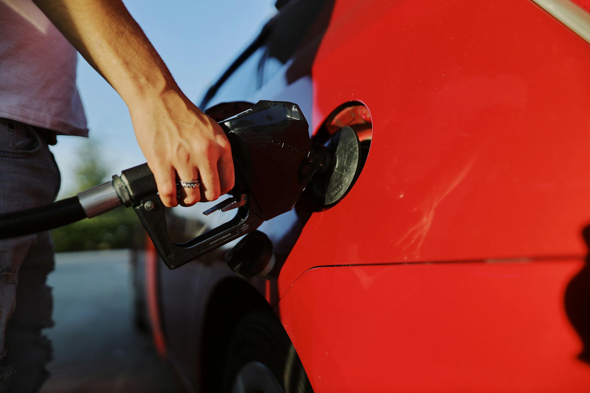 a person filling up a red car with gas